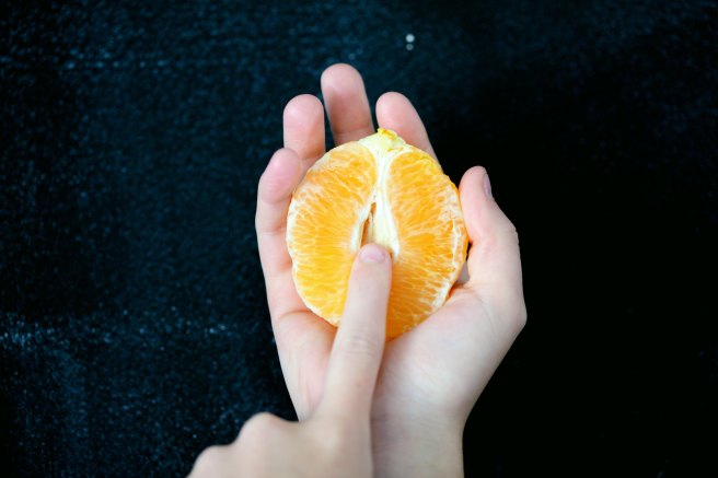 Person holding an orange half with finger in the middle.